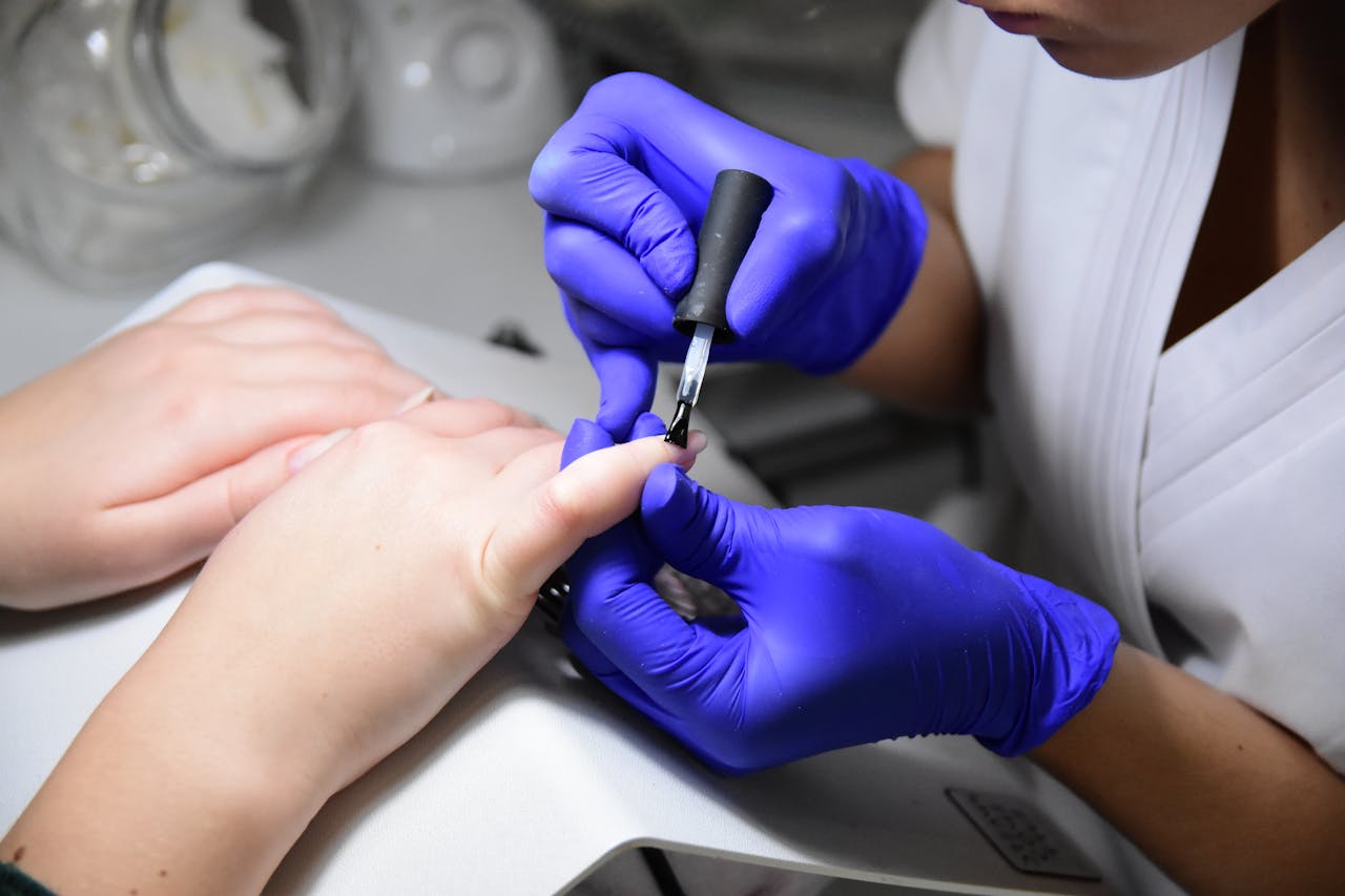 Close-up of a manicurist applying nail polish wearing purple gloves in a salon.