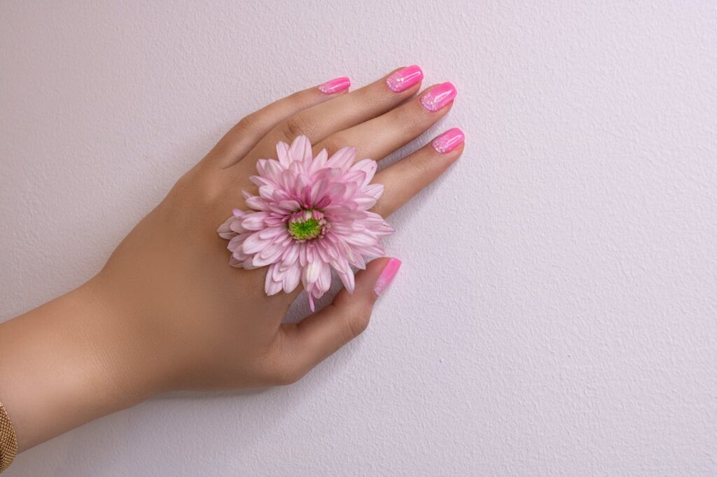 pexels photo 20758448 Close-up of a woman's hand with pink nails and a pink flower, showcasing delicate beauty.