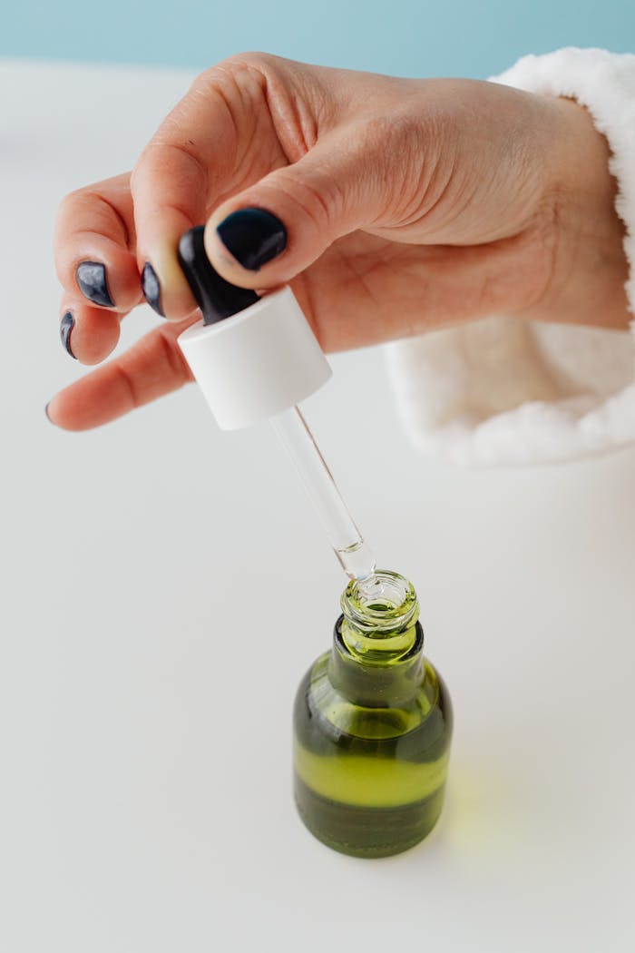A hand with manicured nails uses a dropper to add liquid to a glass bottle.
