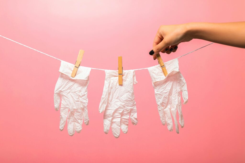 White medical gloves clipped to a line with clothespins against a pink backdrop, symbolizing hygiene.
